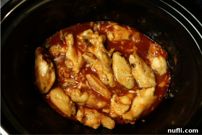 Chicken wings simmering in a rich honey sriracha barbecue sauce within a dark slow cooker bowl.