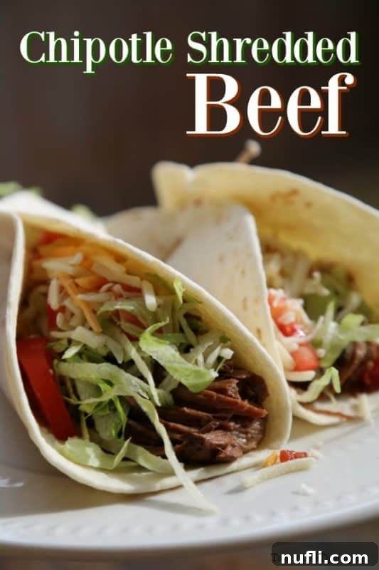 Chipotle shredded beef over two tacos on a white plate, garnished with fresh cilantro and a lime wedge