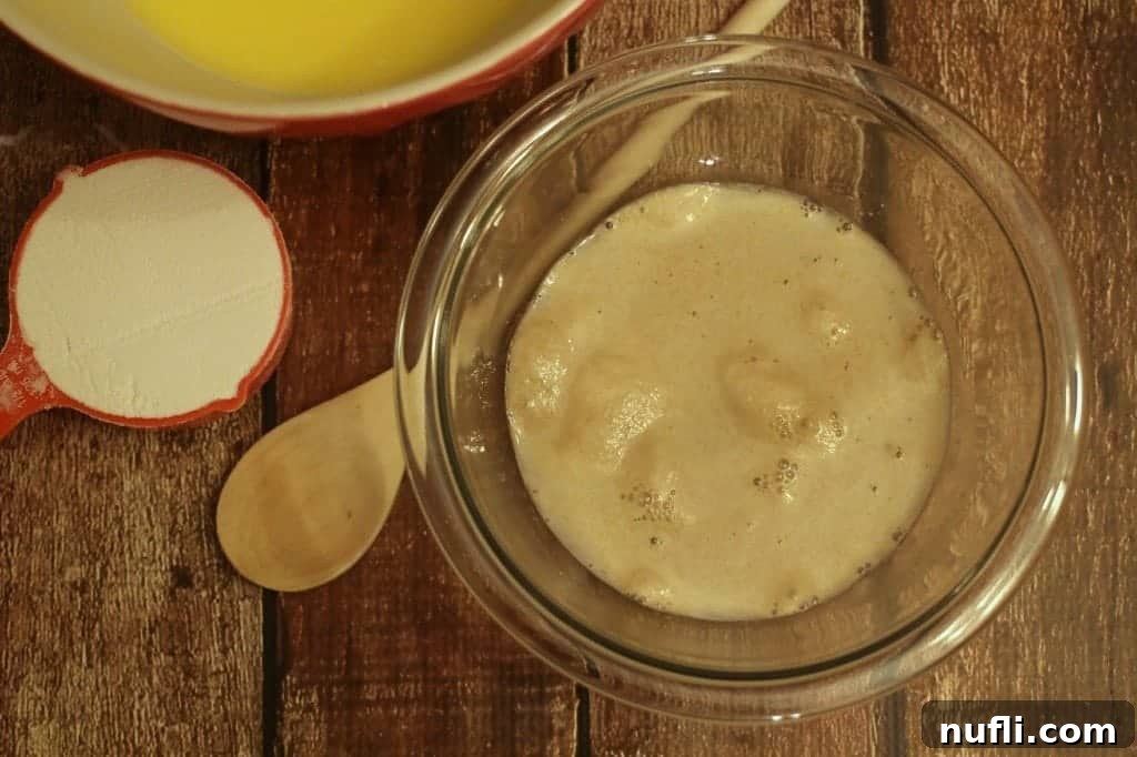 Yeast, water, and sugar mixture foaming in a glass bowl, indicating active yeast.
