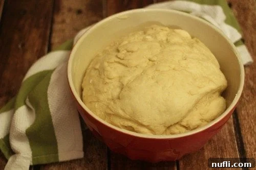 Soft dough, after its first rise, perfectly doubled in size within a red mixing bowl.