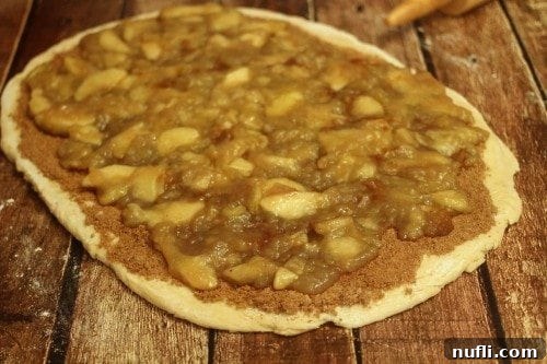 Sweet apple pie filling spread over cinnamon-sugar coated dough, ready to be rolled.