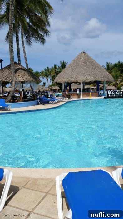 Bayahibe Beach Escape in La Romana, Dominican Republic 4 Inviting resort pool area featuring thatched-roof bars, comfortable lounge chairs, and lush tropical greenery.