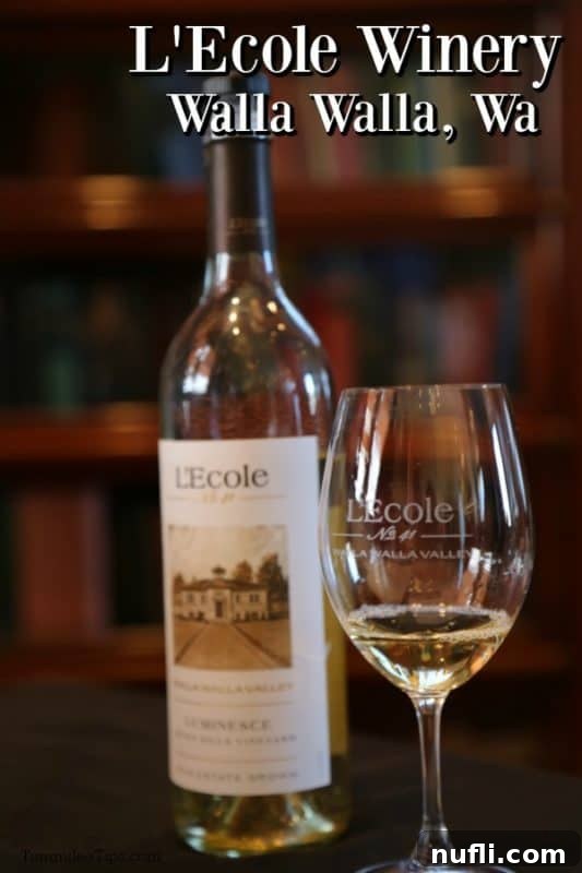 A bottle of L'Ecole Winery's fine wine artfully displayed next to a wine glass, with the picturesque vineyards of Walla Walla in the blurred background, highlighting the region's beauty.