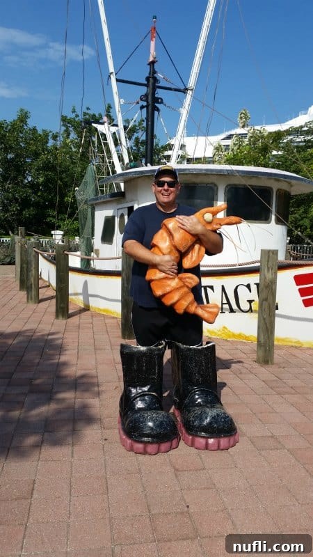 Mahogany Bay Roatan Cruise Adventure 6 John is big fake boots holding a shrimp with a shrimp boat behind him