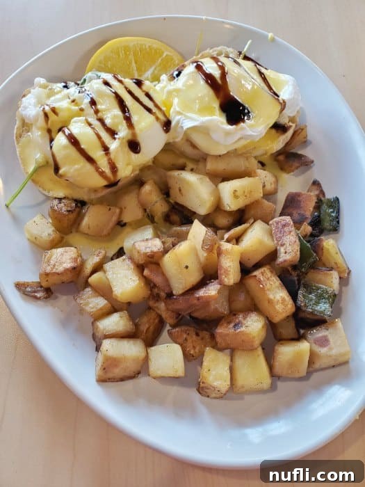 eggs benedict next to homefries on a white plate