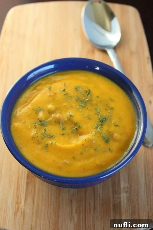 Butternut squash soup in a blue bowl next to a spoon on a cutting board, garnished with fresh herbs.