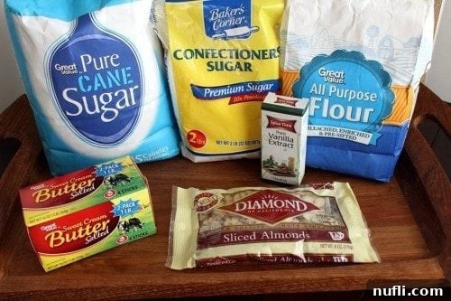 Ingredients for classic Snowball Cookies laid out: sugar, flour, almonds, butter, vanilla extract