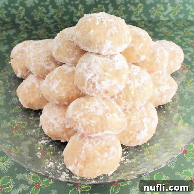 Close-up of freshly baked Snowball Cookies piled on a glass plate, dusted with powdered sugar