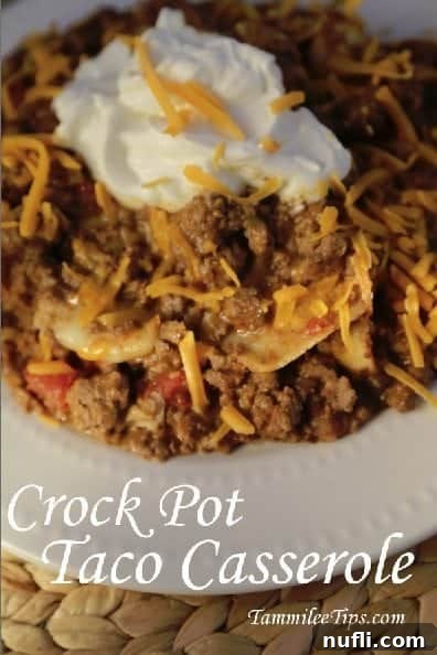 Hearty Crock Pot Taco Casserole served in a white bowl, generously topped with fresh sour cream and shredded cheddar cheese. The rich ground beef and tortilla base is visible beneath the toppings.