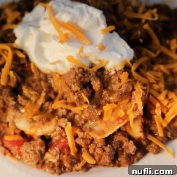 Top-down view of a Crock Pot Taco Casserole dish, richly garnished with melted cheddar cheese and a swirl of sour cream, ready to be served.