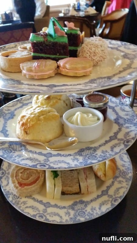 A grand tea service display with a three-tiered plate filled with scones, desserts, and an assortment of tea sandwiches, alongside a teapot and teacup.