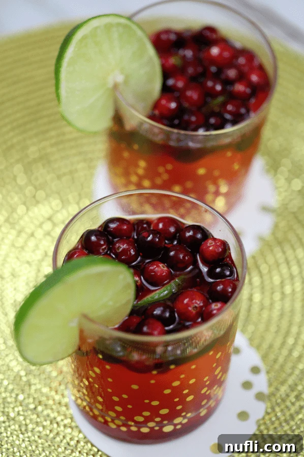 A festive Cranberry Lime Cocktail in elegant gold polka dot glasses, garnished with a fresh lime wheel and floating cranberries, perfect for holiday celebrations.
