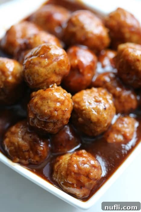 Close-up of cranberry barbecue meatballs in a white serving bowl, garnished for presentation.