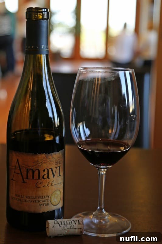 An Amavi Cellars wine bottle elegantly standing beside a half-filled glass of wine, set against a soft, inviting background