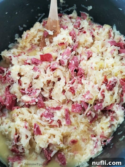 Easy Crock Pot Reuben Dip 4 A dark slow cooker filled with bubbling hot Reuben dip, ready to be served, with a wooden spoon resting inside.
