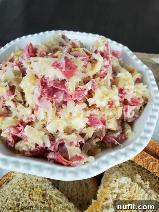 Easy Crock Pot Reuben Dip 5 A white bowl filled with creamy Reuben dip, surrounded by an assortment of toasted rye bread triangles and crackers, ready for serving.