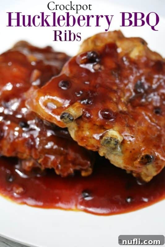 Succulent Crockpot Huckleberry BBQ Ribs piled high on a white plate, showcasing their rich, glossy sauce.