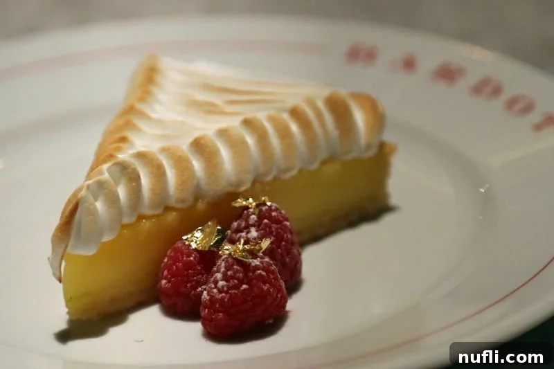 A vibrant lemon meringue tart alongside fresh raspberries dusted in gold, beautifully arranged for dessert.