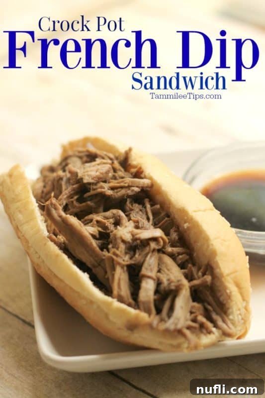 A perfectly cooked Crockpot French Dip Sandwich in a bun on a white plate, served alongside a small bowl of savory Au Jus sauce for dipping.