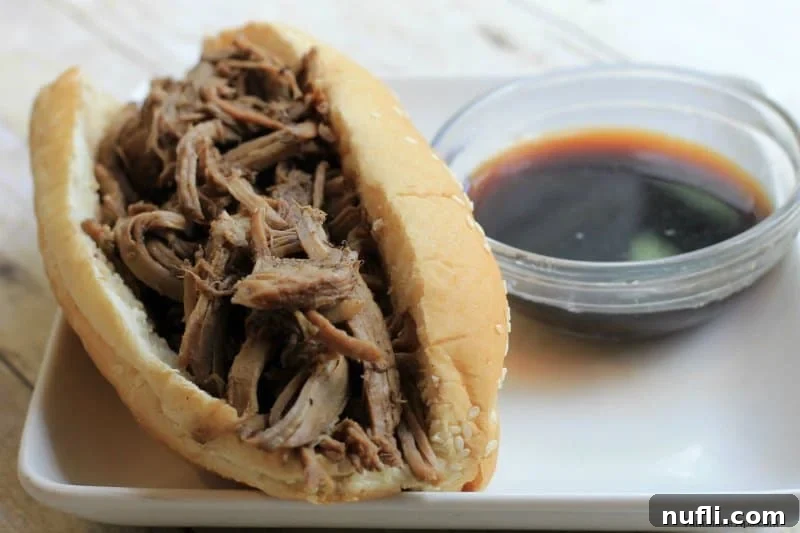 A delicious Balsamic French Dip sandwich served in a toasted bun on a white plate, with a small bowl of rich Au Jus sauce beside it, ready for dipping.