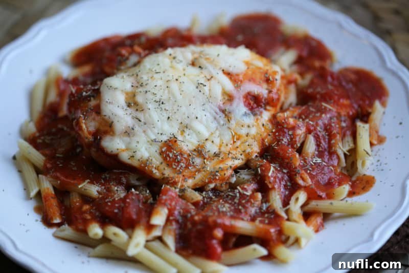 Chicken parmesan on a white plate with penne pasta and sauce