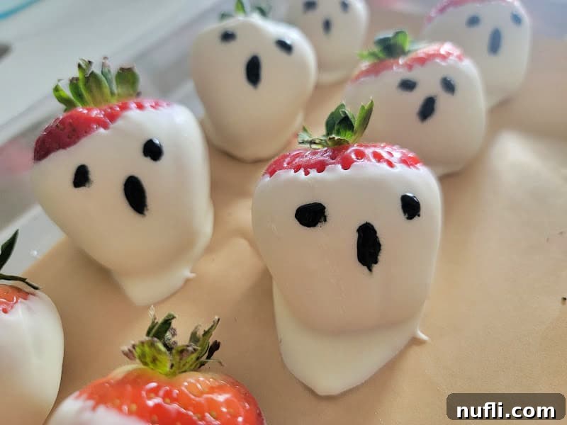 Adorable ghost-shaped strawberries meticulously arranged on a sheet of parchment paper, ready to spook and delight.
