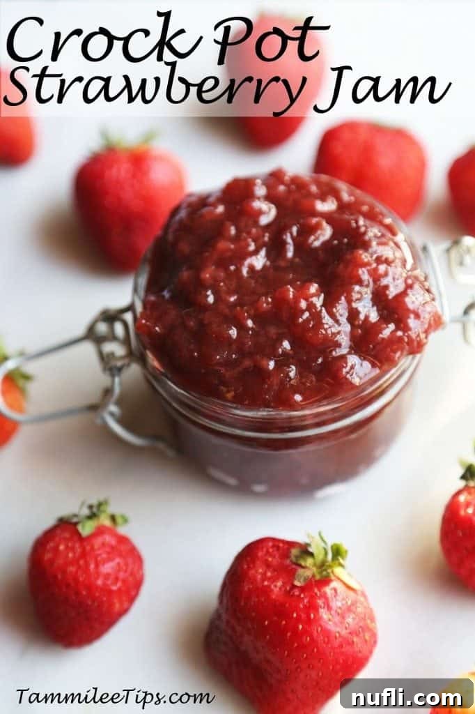 A glass jar filled with homemade Crockpot Strawberry Jam, beautifully displayed alongside fresh strawberries, emphasizing its natural goodness.