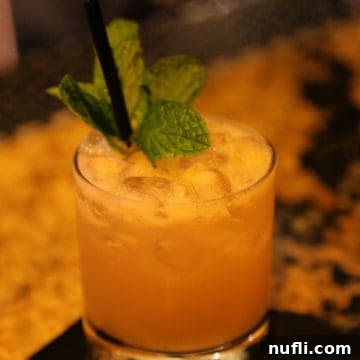 A vibrant Mai Tai cocktail with a fresh mint leaf garnish in a stylish rocks glass, against a dark background, inviting a refreshing sip.