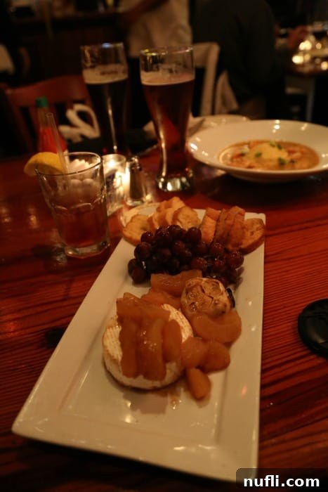A gourmet appetizer featuring brie cheese artfully arranged with dried fruits and nuts on a white plate, served at Crescent City Brewhouse.