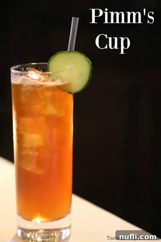 Pimm's Cup cocktail in a tall glass with a fresh cucumber wheel garnish and a straw, ready to be enjoyed.