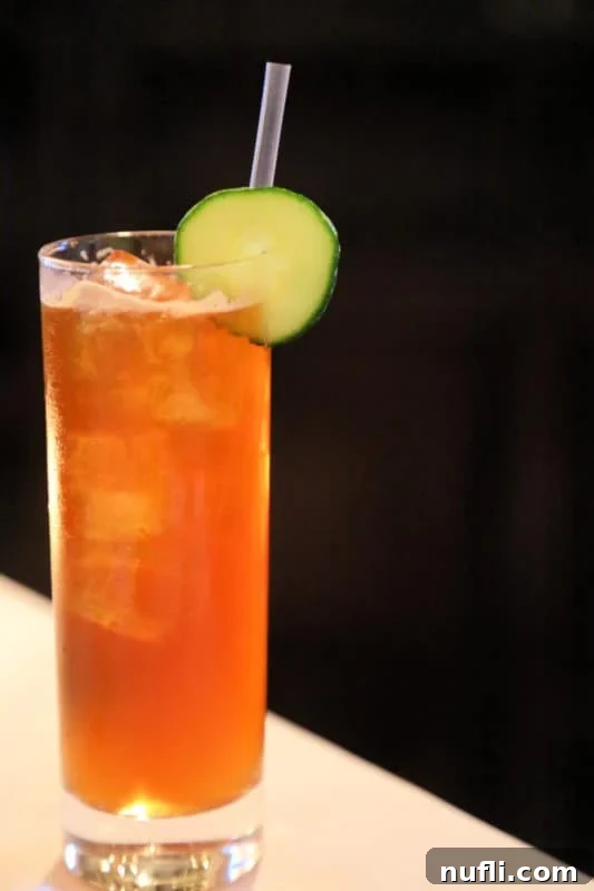 Close-up of a Pimm's Cup cocktail in a tall glass, garnished with a cucumber wheel and a straw, on a dark background.