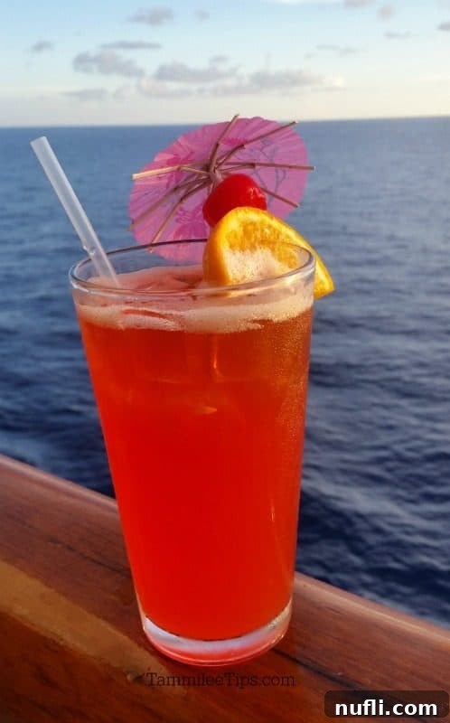 Another view of a Caribbean Breeze cocktail on a cruise ship rail, with the blue ocean stretching out to the horizon, emphasizing its perfect setting.
