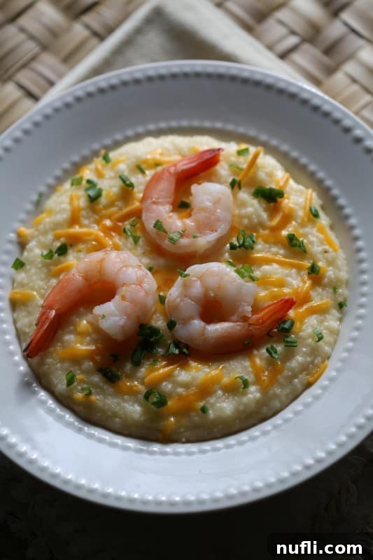 Crockpot Shrimp and Grits in a white bowl with green onion and cheddar cheese garnish