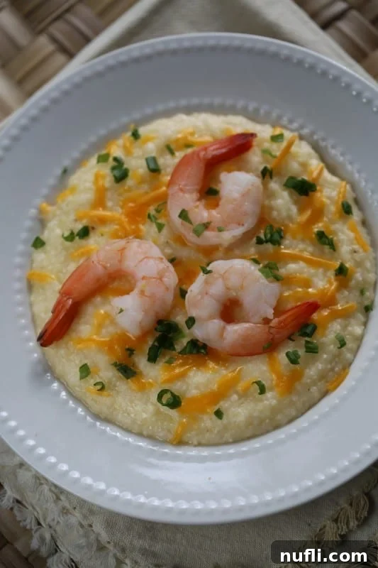 Crockpot Shrimp and Grits in a white bowl with green onion and cheddar cheese garnish