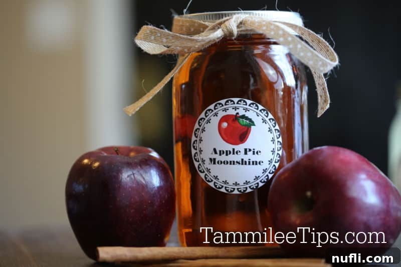 Apple pie moonshine jar next to apples and cinnamon sticks
