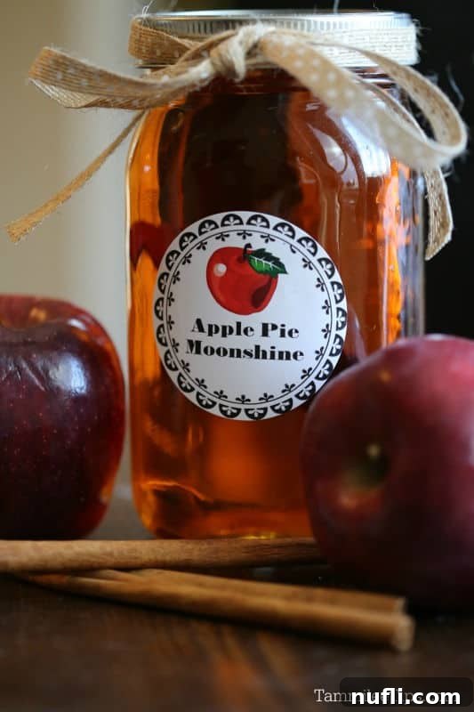 apple pie moonshine label on a jar next to apples and cinnamon sticks