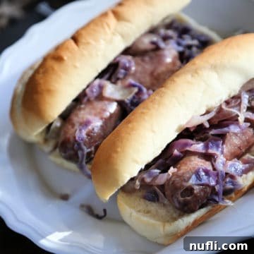 Savory Slow Cooker Beer Brats 3 beer brats with cabbage on buns on a white plate