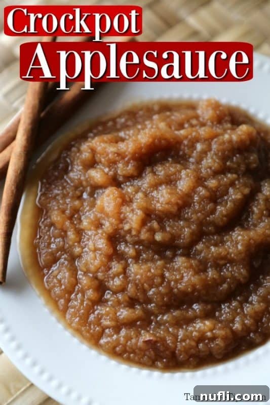 Homemade Crockpot Applesauce in a white bowl, garnished with cinnamon sticks.