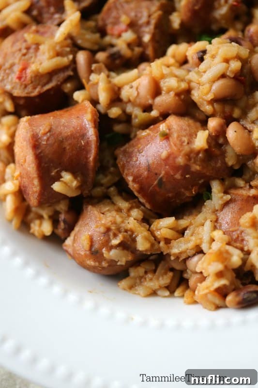 A white plate piled high with flavorful rice, kielbasa slices, and black-eyed peas, forming a delicious Hoppin John dish.