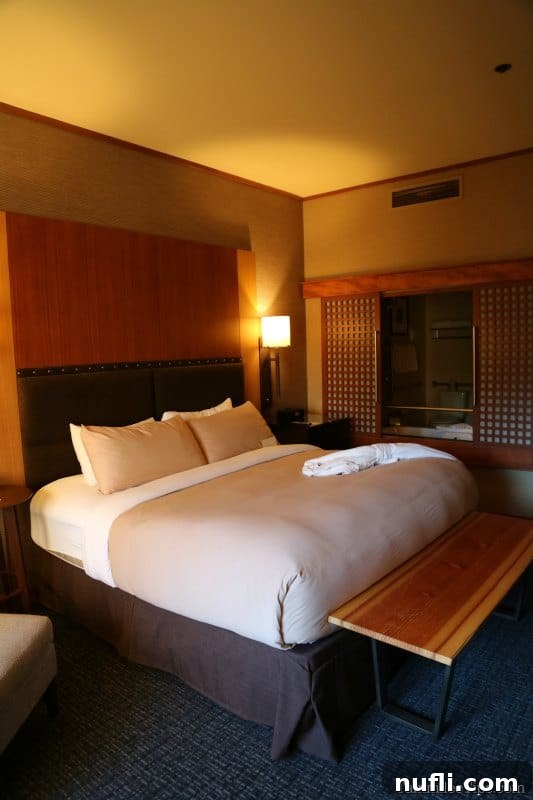 King bed with comfy linens next to a wooden bench and chair 