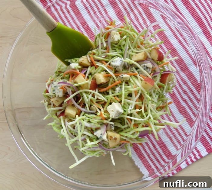 Broccoli slaw ingredients in a glass bowl with a spatula next to a red napkin