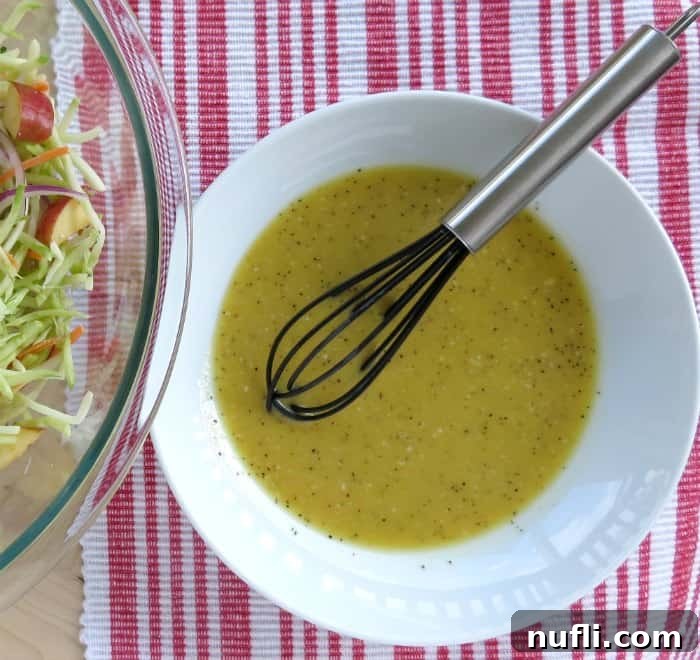broccoli slaw dressing in a white bowl with a black whisk