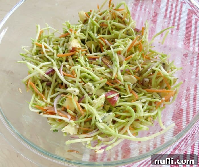 broccoli slaw in a glass bowl next to a red cloth napkin