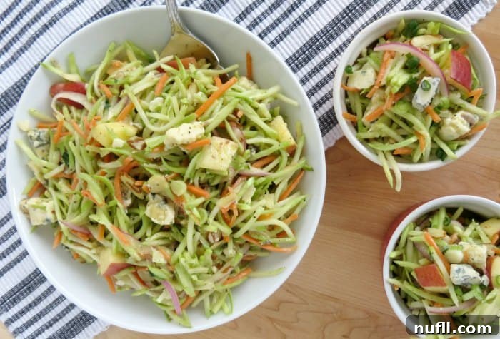 broccoli slaw in a white serving bowl with a silver spoon next to two smaller bowls on a striped napkin