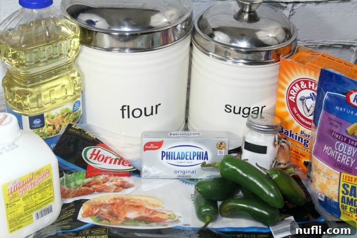 Assortment of ingredients for Bacon Jalapeno Cheese Bread including flour, sugar, baking soda, cheese, jalapenos, cream cheese, bacon, and oil displayed on a kitchen counter