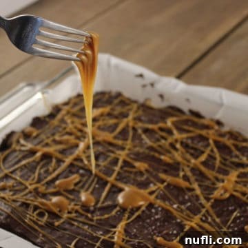 Salted Caramel Rice Krispie Treat in a parchment lined paper with a fork dripping in caramel
