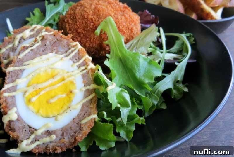 Two golden brown Scotch eggs with a crispy panko coating, arranged on a dark plate with a fresh garnish of arugula leaves.