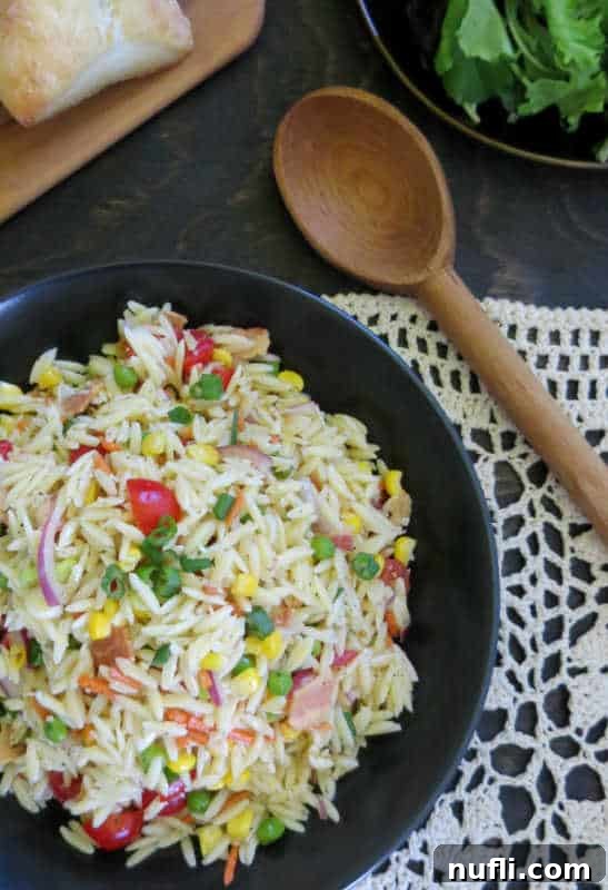 Orzo salad in a dark bowl next to a wooden spoon and plate of bread