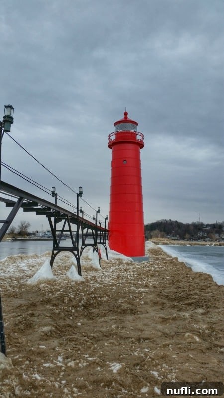 The Grand Haven Lighthouse covered in thick ice, showcasing its resilience against the harsh Michigan winter, with a frozen pier stretching towards it.
