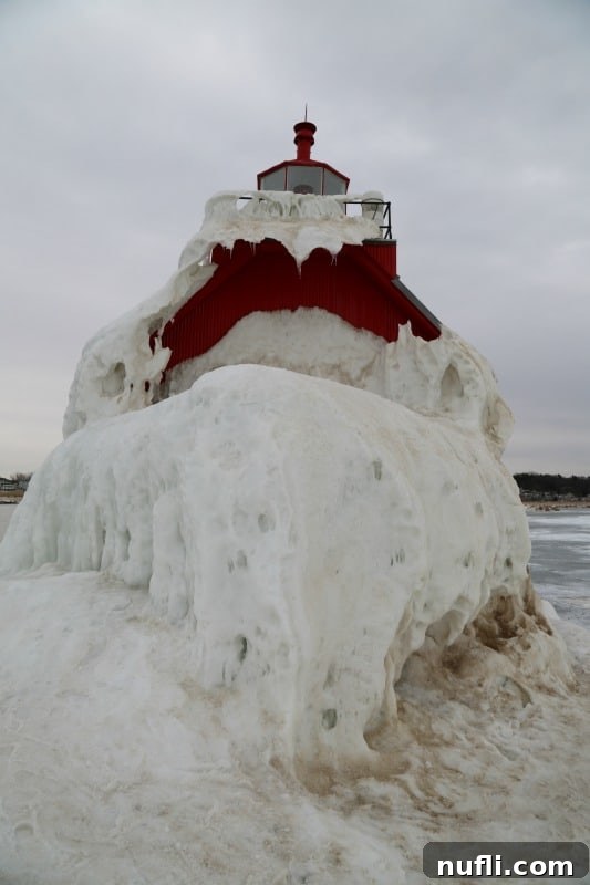 The Grand Haven Lighthouse heavily encrusted in thick, rough ice, creating a breathtaking and formidable winter spectacle.